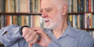 现代高级男士在家使用智能手表。退休人士在图书馆上网浏览和聊天