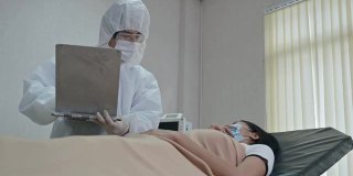 亚洲男性医生在隔离病房的病床上检查流感患者的症状并在检查表上写下信息