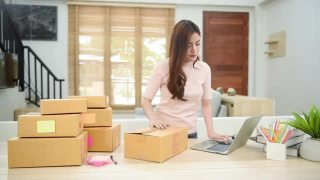 一个漂亮的亚洲女人检查订单并把它们装进纸盒用笔记本电脑是一种在线业务在家工作是新常态视频素材模板下载