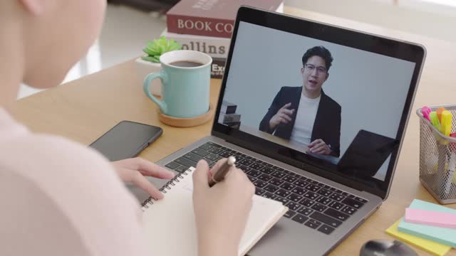 后视图年轻的亚洲女性听观看数字课程在线学习员工技能在笔记本电脑在家庭办公室的工作场所。针对成人的商学院课程教育。