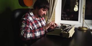 一个穿着格子睡衣的男人晚上在他的家庭办公室里用打字机打字。