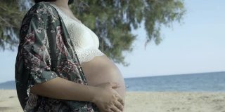 一名孕妇站在海滩上抚摸着自己的肚子。