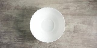巧克力麦片戒指在慢镜头中掉进一个白色的碗里，碗放在一张木桌上