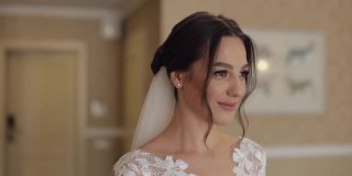 可爱的新娘穿着白色婚纱和面纱呆在家里的客厅里，看着镜头，微笑着
