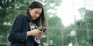 年轻的亚洲女性办公室经理在商业区用智能手机输入社交媒体信息。成功。业务人员。技术。