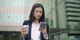 年轻的亚洲女性办公室经理在商业区用智能手机输入社交媒体信息。成功。业务人员。技术。