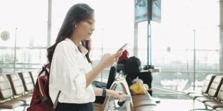 亚洲女性在机场行走和使用智能手机