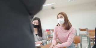 在大学教室里，一位老师用平板电脑给学生上课。学生戴口罩预防病毒新常态。