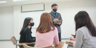 在大学的教室里，老师站在教室的前面教学生。学生戴口罩预防病毒感染。
