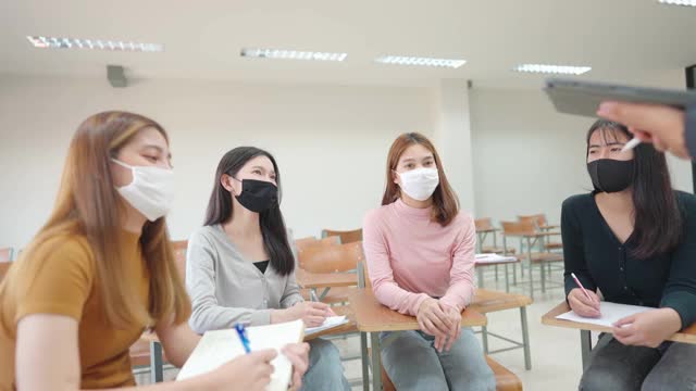 在大学教室里，一位老师用平板电脑给学生上课。学生戴口罩预防病毒新常态。