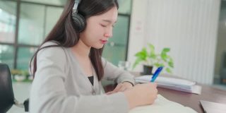 一名年轻的亚洲大学生戴着耳机在家在线学习，在病毒爆发期间没有上大学。