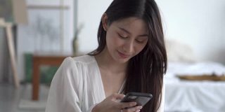年轻的亚洲女性在卧室里使用手机