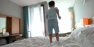 亚洲小孩跳上酒店的卧室。旅游和度假的概念