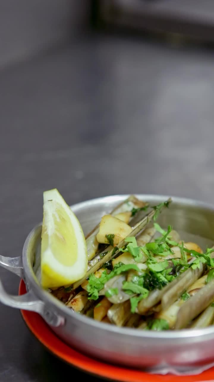开胃的蛤蜊配上大蒜、香草，放在一个铝制的盘子里，再点缀上一打柠檬。垂直视频。特写镜头。