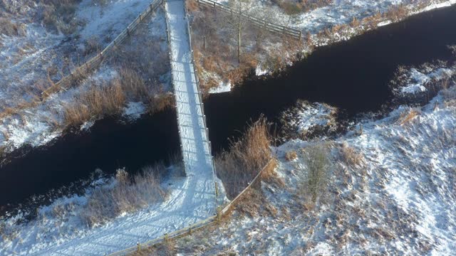 从空中俯瞰，一座木桥穿过一条小河，在一个霜雪过后的早晨加入一条小径