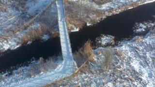 从空中俯瞰，一座木桥穿过一条小河，在一个霜雪过后的早晨加入一条小径视频素材模板下载