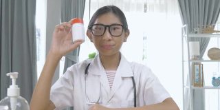 亚洲药剂师女孩在家里通过视频电话解释药瓶，封锁生活方式的概念。