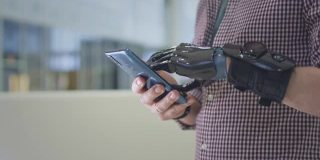 一个戴着假肢的年轻人正在使用智能手机。一个没有手的残疾人在电话上写一条信息或者在网上购物。肢体修复术的未来概念。