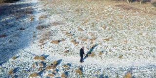 这是一架无人机拍摄的鸟瞰图，拍摄的是一位老人独自走在苏格兰西南部一条被雪覆盖的人行道上