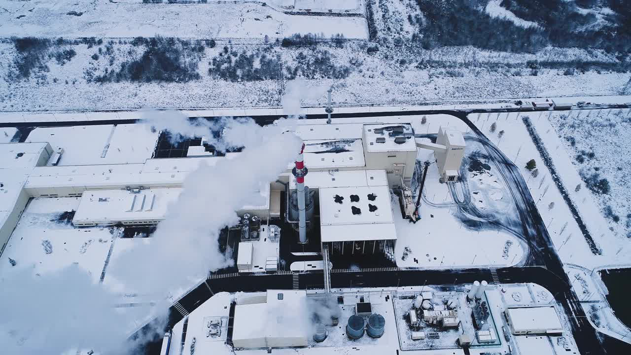 工厂下着雪，冬天里。我们可以看到一股烟从烟囱里冒出来，建筑物上覆盖着雪