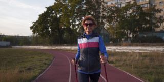 年龄成熟，积极的生活方式和健康。快乐的退休妇女带着拐杖绕着城市体育场。成熟的女性在户外进行北欧漫步。老年女运动员与徒步手杖行走。