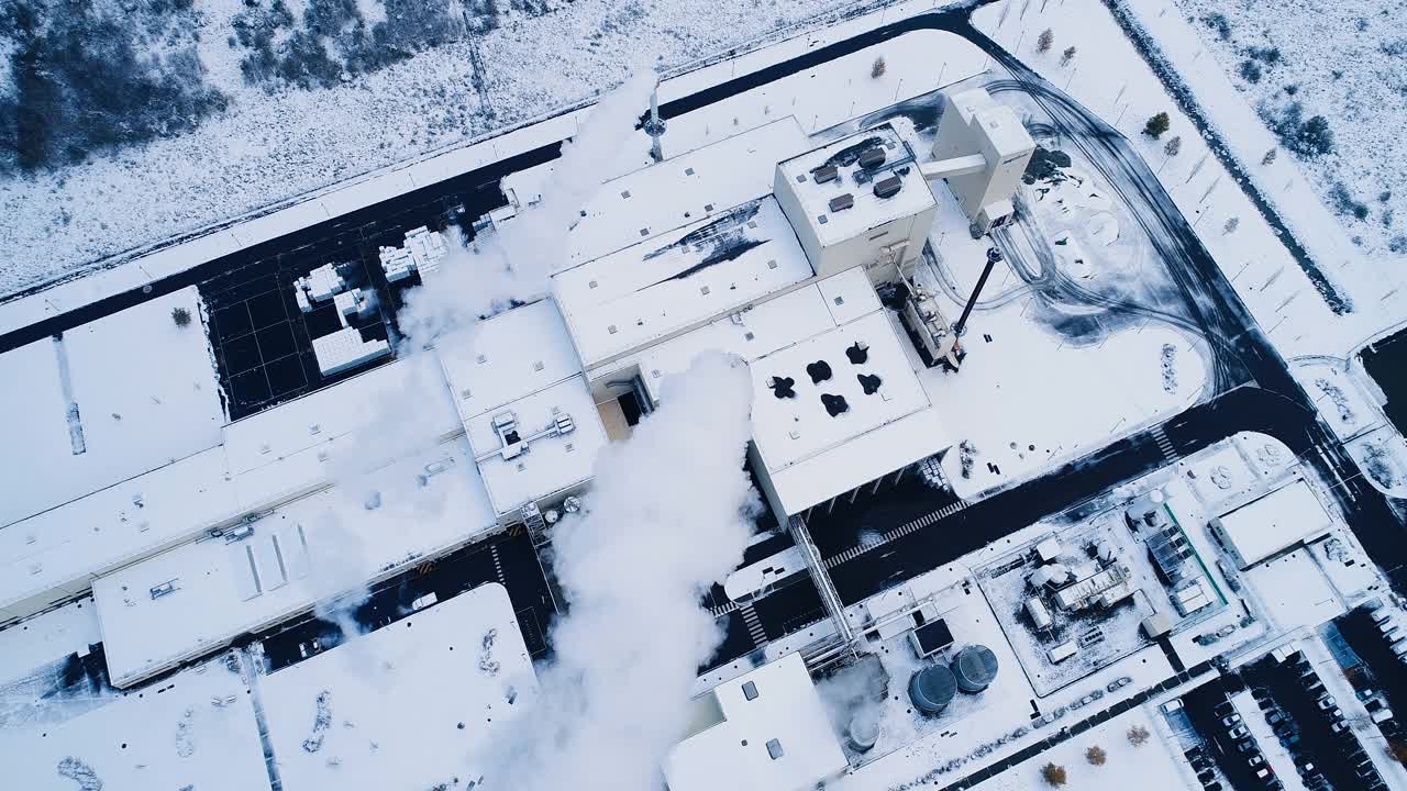 一架无人机俯瞰积雪下的工厂。我们可以看到烟从烟囱里冒出来