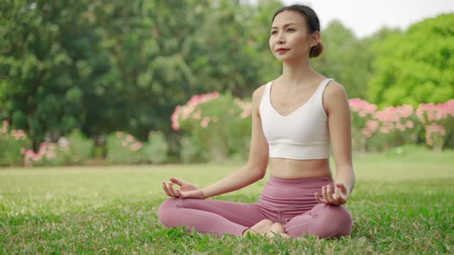 一位年轻的亚洲女子坐在花园里练瑜伽，她很放松，很享受锻炼。