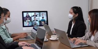 年轻的亚洲员工和资深的办公室员工团队通过电脑进行Zoom视频电话会议，商务人士共用办公桌使用电脑共同工作