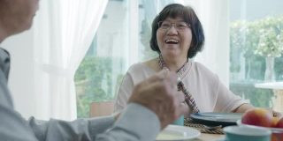 迷人的年轻老年亚洲公民夫妇幸福的坐在餐桌上，聊天，吃汤的健康营养早餐餐在日常生活方式在老亚洲护理居家护理。
