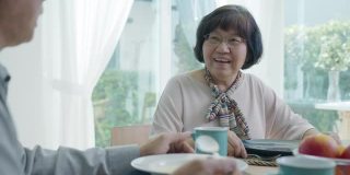 迷人的年轻老年亚洲公民夫妇幸福的坐在餐桌上，聊天，吃汤的健康营养早餐餐在日常生活方式在老亚洲护理居家护理。