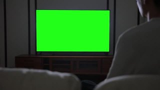 男人在看绿色屏幕的电视视频素材模板下载