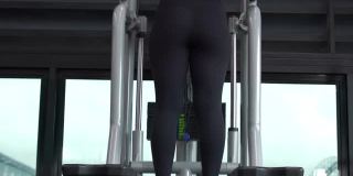一个女人在健身房独自训练，她似乎在酒吧里做引体向上