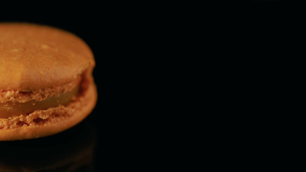 橙色法式马卡龙，黑色背景。美味的传统法国甜点近距离