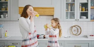 快乐的小女孩和她的妈妈在厨房享用新鲜可口的冰沙，并互相击掌庆祝