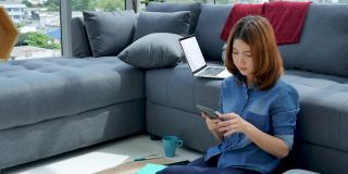 妇女在家工作的笔记本电脑在线会议在家庭办公室。亚洲女企业家用笔记本电脑坐在沙发上科技新常态的生活方式。快乐的女人打字键盘笔记本电脑
