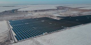 在冬天有雪的田野和山丘之间的巨大太阳能农场里有数百块蓝色的太阳能板