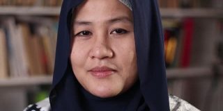 年轻的亚洲穆斯林女子站在图书馆里对着镜头说话，商人在做视频会议