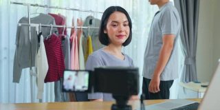 新冠肺炎疫情期间，亚洲年轻夫妇在线直播销售产品。电话销售时，女士向顾客展示布料，并提供细节。远程采购和采购技术概念。