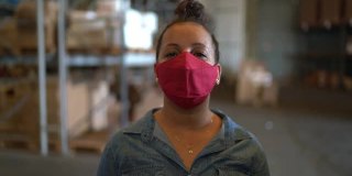 一个戴着面罩的女人在一个配送仓库里进行商业视频通话-从摄像头角度