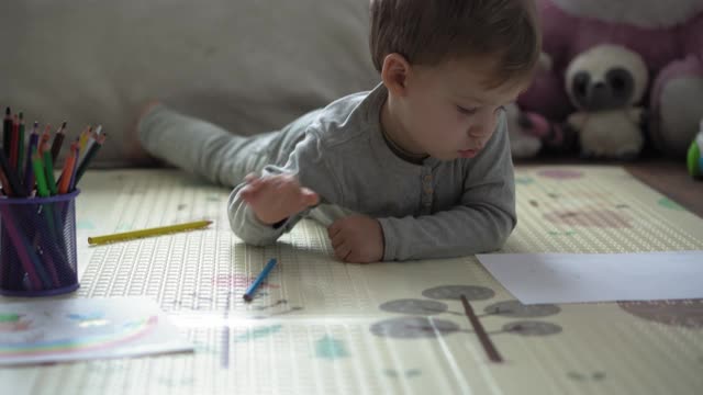 童年，艺术，教育，创意概念-真实的学前聪明的创意天才男孩2-4岁用彩色铅笔画家庭的春天夏天，彩虹在家里的垫子地板上
