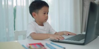 亚洲幼儿园男孩视频会议电子学习与老师在客厅的笔记本电脑在家里。在家教育、远程学习、在线教育和教育可以预防COVID-19病毒。