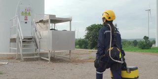 亚洲妇女检查工程师戴着安全带和安全线在泰国风电场准备和检查风力发电机的安全。