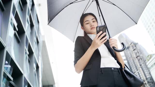 年轻的亚洲商务女性带着雨伞走在城市里，雨季。