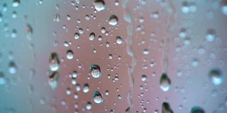 大雨滴落在玻璃窗的背景上。在雨天，水滴在玻璃上流动的慢动作。微距镜头。