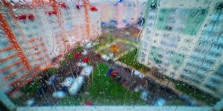 水滴在城市背景的玻璃上流淌。多雨的天气。雨点落在玻璃窗上。水滴沿着玻璃移动。