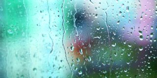 雨水把窗户打湿了。水滴在模糊视图背景上的玻璃窗口上向下移动。特写镜头。