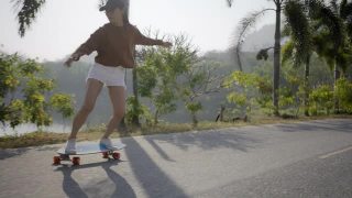 亚洲妇女在美丽的夏天在户外冲浪或滑冰。快乐的年轻女子早上在公园玩冲浪滑冰。体育活动生活方式概念。视频素材模板下载