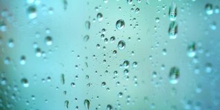 美丽的蓝色背景与雨滴。在雨天，透明的水滴落在玻璃窗上。特写镜头。