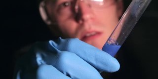 一位年轻的科学家兴奋地在试管中检查这种物质。化学实验室在黑暗中。