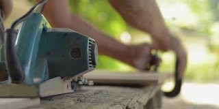 老人木匠用电动刨床刨木板。在家里工作。DIY工匠和木工概念。在车间从事木工生产家具的模糊木匠。